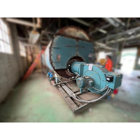Cleaver Brooks 700HP industrial gas burner showing combustion air fan motor, skid-mounted assembly, gas train piping, and control panel on Burnham boiler prior to removal