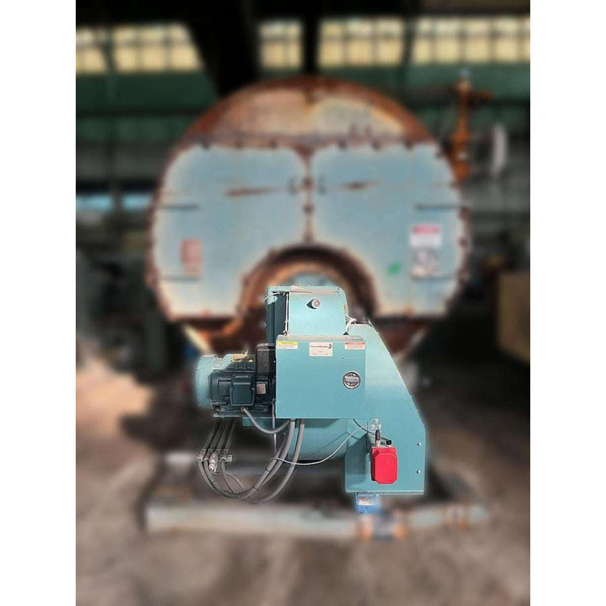 Cleaver Brooks 700HP industrial gas burner front view showing combustion air motor, teal housing, red emergency disconnect switch, and Burnham 700HP boiler front in background