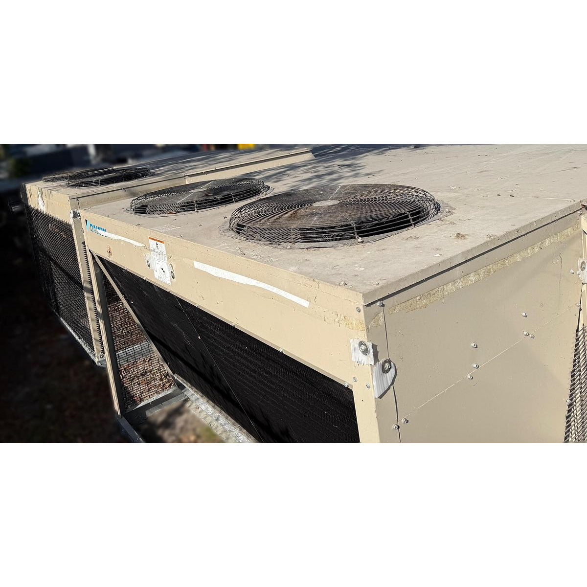 Daikin DPS012AHHE2DW-4 rooftop HVAC unit top view showing dual condenser fan motors with wire guards, beige powder-coated cabinet, and condenser coil section