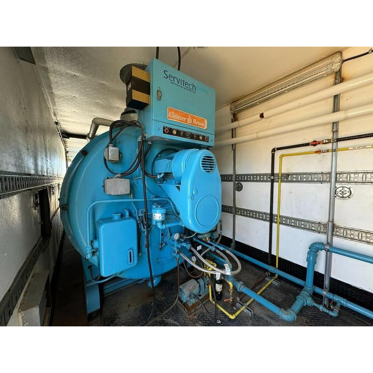 Blue industrial machine with 'Servitech' branding in a mechanical room.