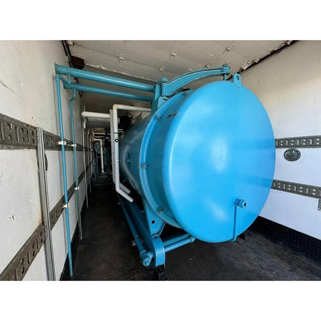 Large blue cylindrical tank inside a building with white walls and gray floor.