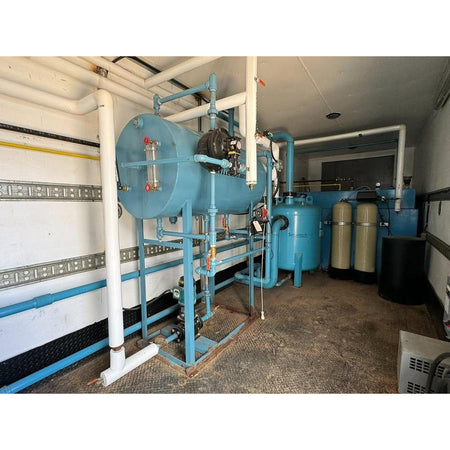 Industrial water treatment system with blue tanks and pipes in a room.