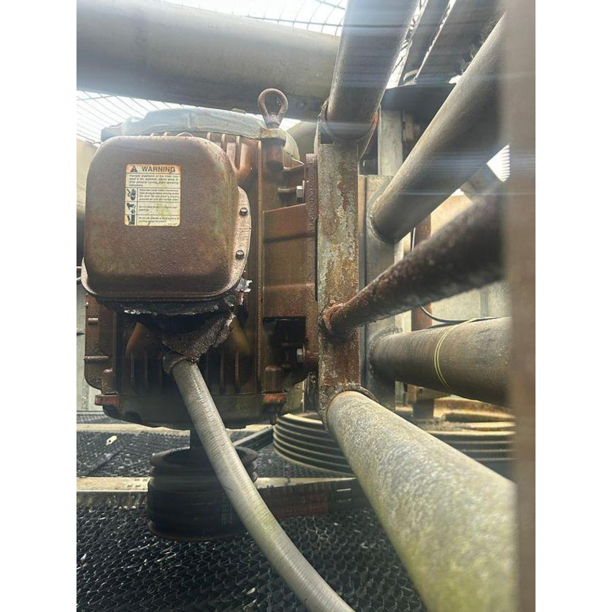Rust-covered mechanical component with warning label in an industrial setting