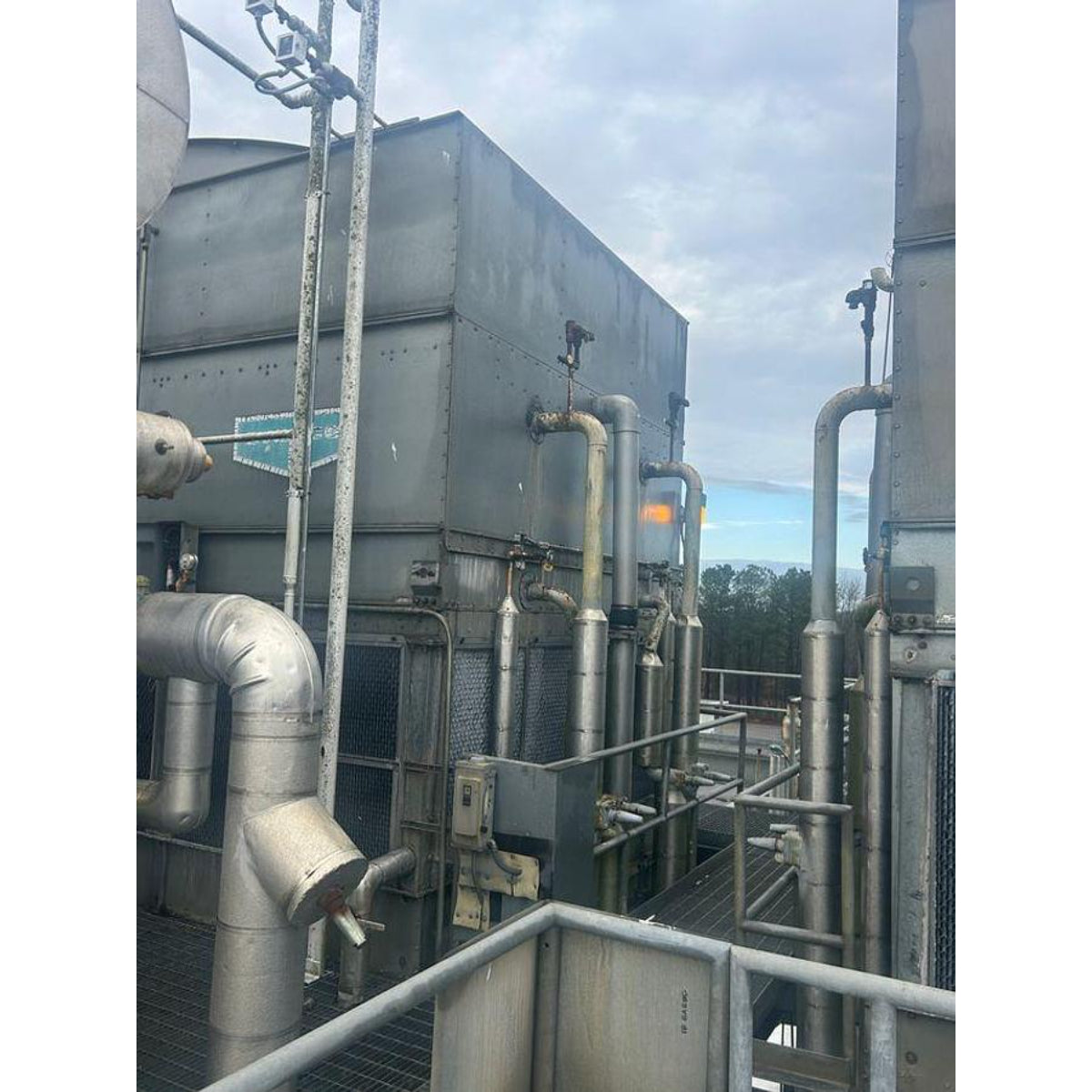 Industrial cooling tower with piping and equipment against a cloudy sky