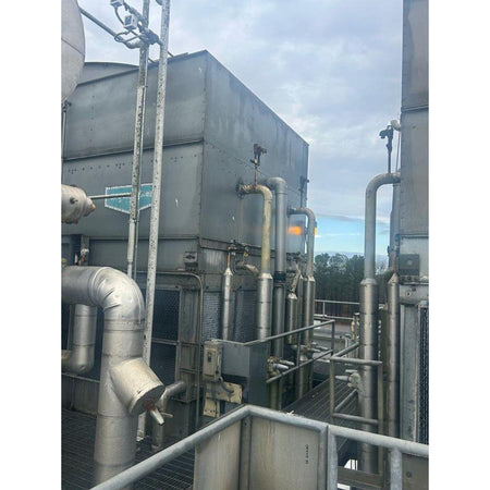 Industrial cooling tower with piping and equipment against a cloudy sky