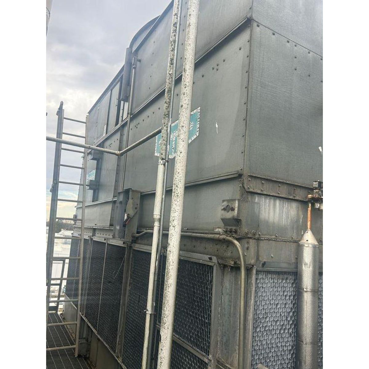 Large industrial cooling tower with metal structure and pipes against a cloudy sky.