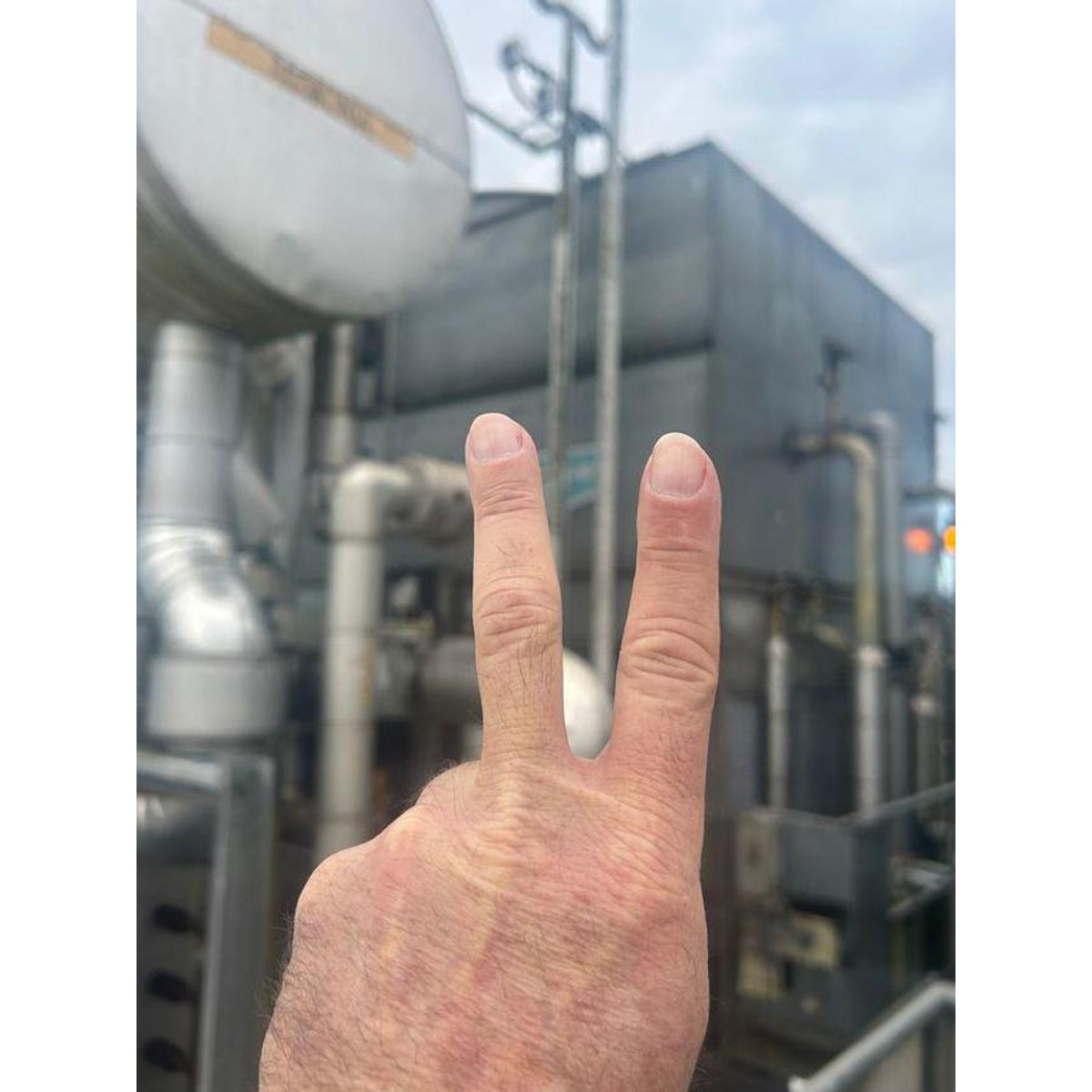 Hand making a peace sign in front of industrial equipment