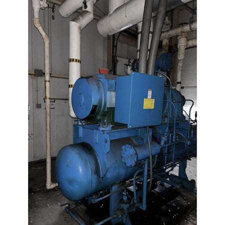 Large blue industrial machine with pipes and valves in a mechanical room.