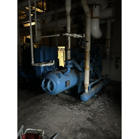 Industrial refrigeration system with blue compressor and pipes in a dimly lit room.