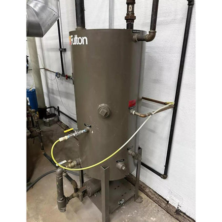 Brown industrial tank with 'Fulton' branding, connected to various pipes and hoses, on a concrete floor.
