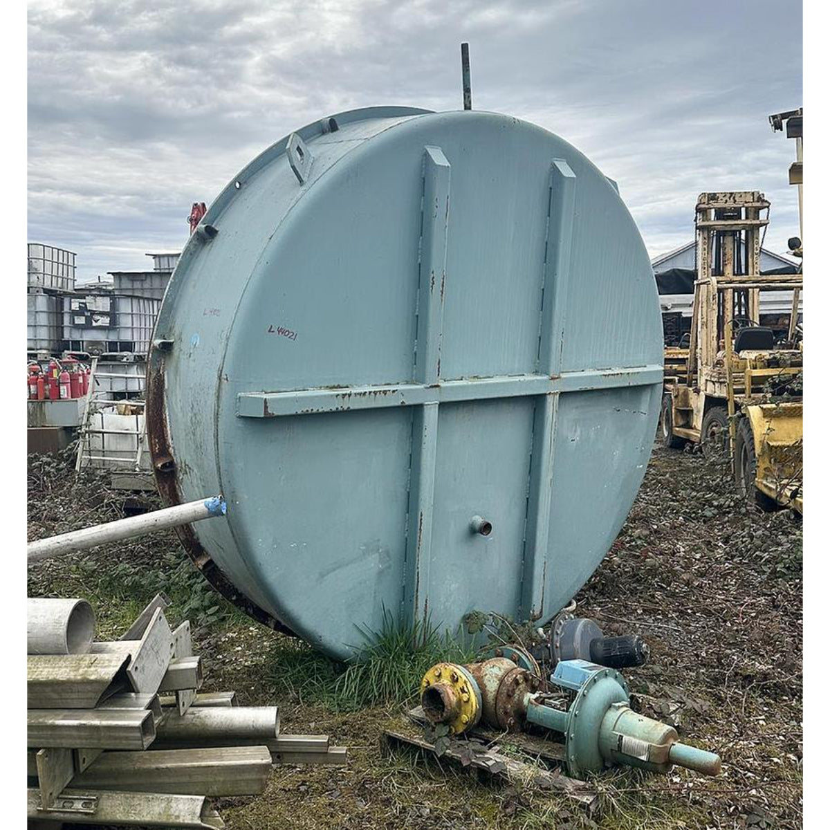 Large cylindrical metal tank on a construction site with equipment and debris around.