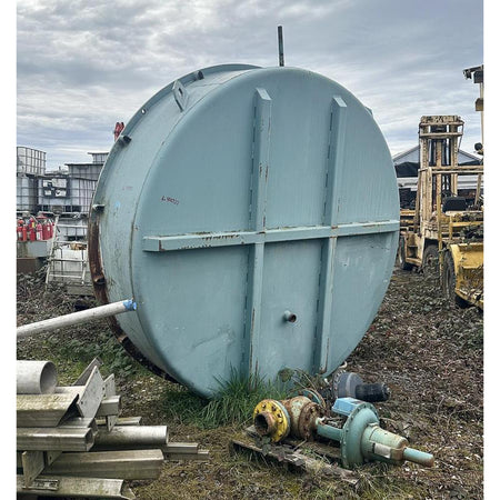 Large cylindrical metal tank on a construction site with equipment and debris around.