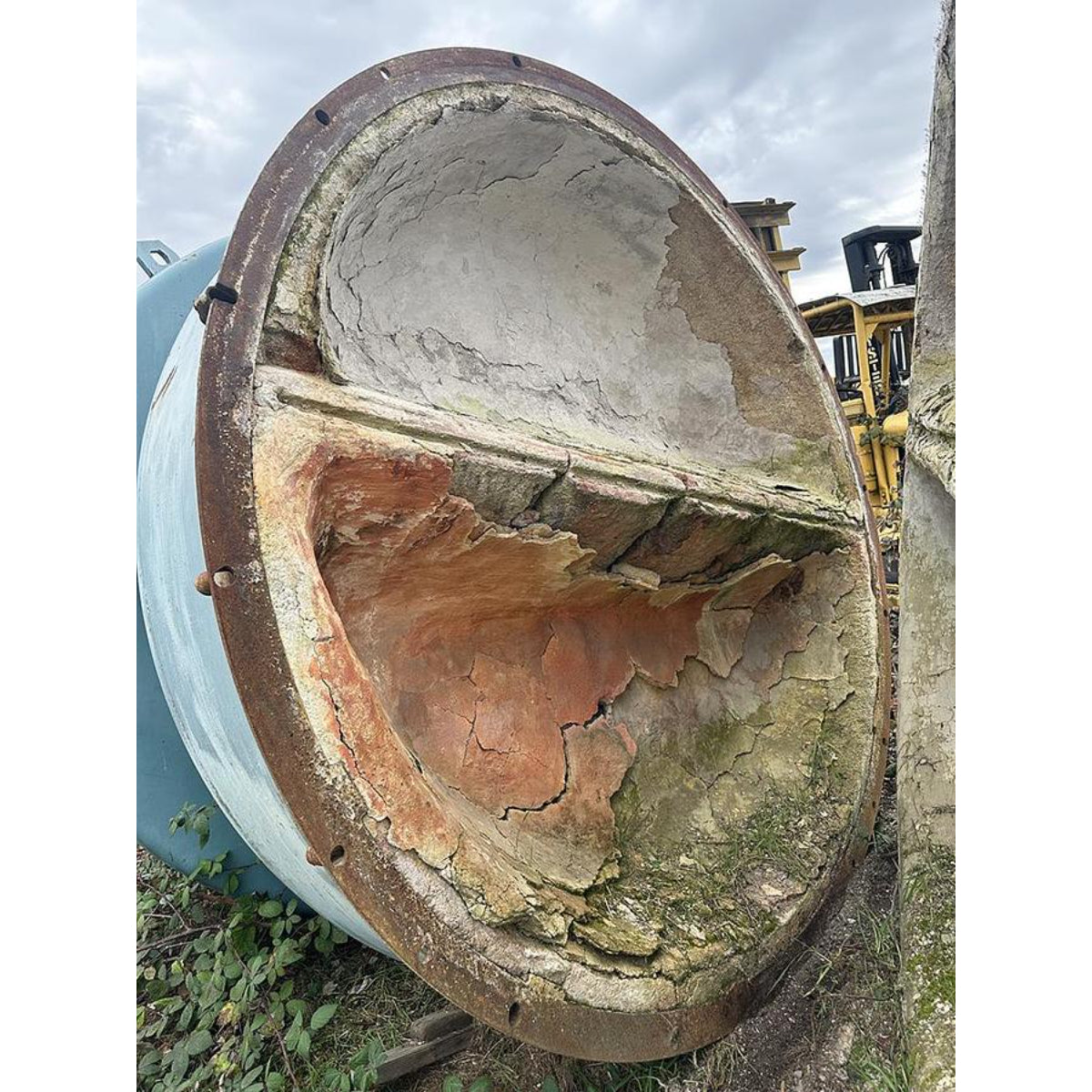 Rust-covered metal cylinder with a large hole in it, outdoors.