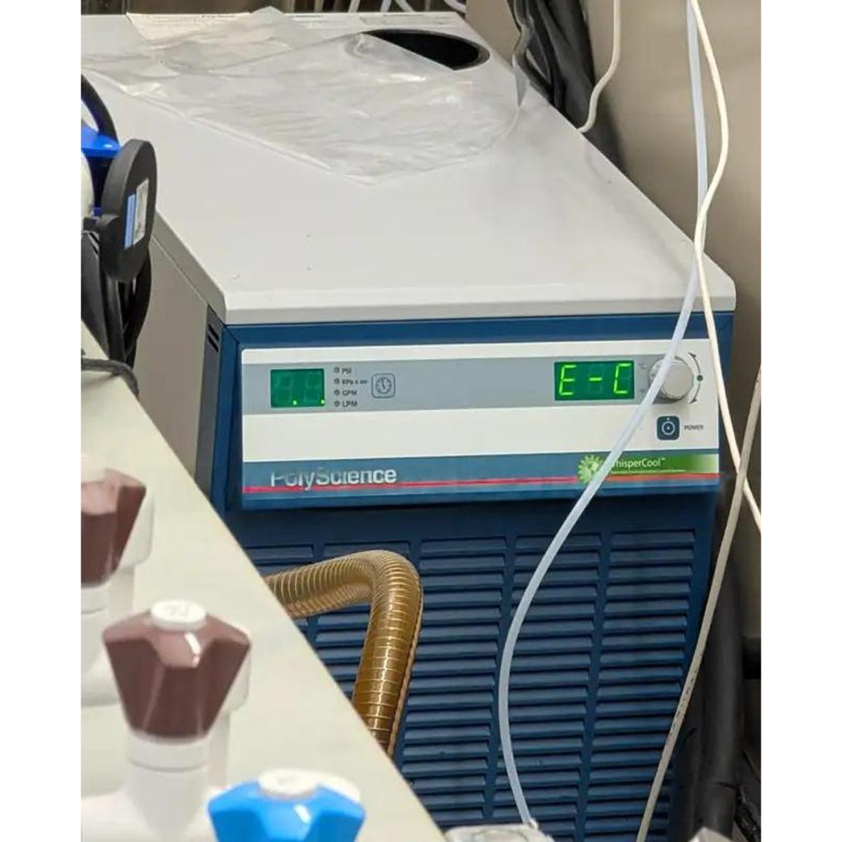PolyScience WhisperCool recirculating chiller unit showing active green LED displays on the front panel control interface, with coolant tubing connected, power button visible, and the blue and white unit housing in a laboratory setting