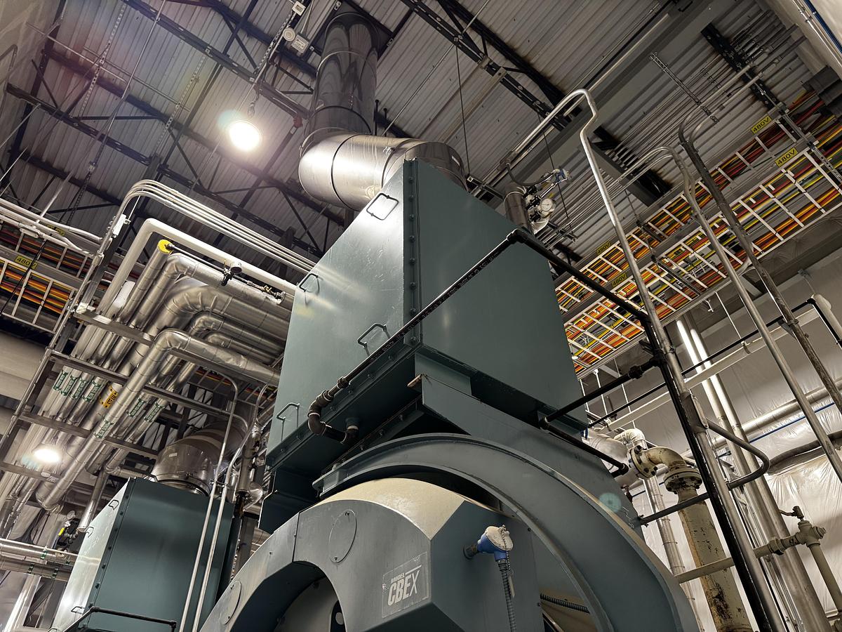 Large industrial machine in a factory setting with visible pipes and ceiling.
